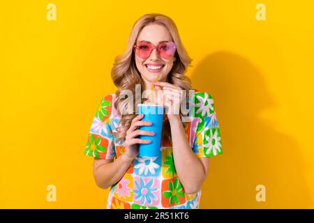 Photo pretty cheerful lady visit movie premiere drink soda paper cup wear heart sunglass print shirt isolated yellow color background Stock Photo