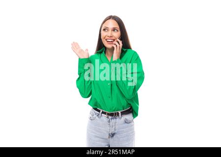 portrait of a smart pensive slim cute brown-eyed brunette woman dressed in a green shirt chatting on the phone on a white background with copy space Stock Photo