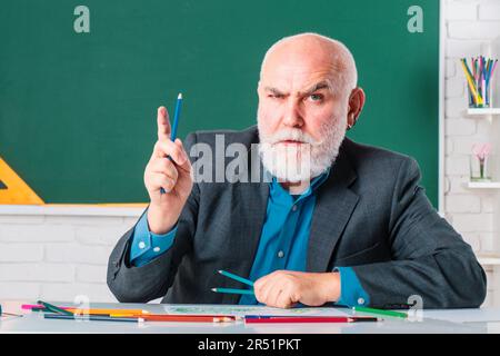 Serious professor. Education and knowledge concept. Elderly professor, teacher on blackboard. Senior professor, teacher in classroom. Funny professor Stock Photo
