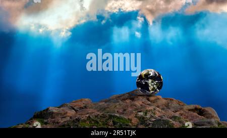 The planet earth on a rock against a dramatic blue sky with shards of sunlight filtering through the clouds Stock Photo