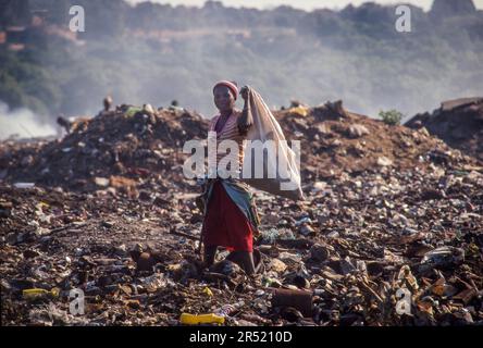 Mozambique, Maputo; Woman is standing on a garbage dump, surrounded by smoke. Stock Photo