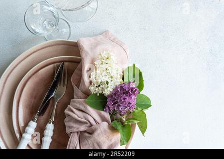 Top view of cropped table setting with lilac flowers on tableware in dust pink color on white surface with empty glasses Stock Photo
