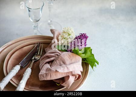Front view of Spring table setting with lilac flowers on tableware in dust pink color on white surface with empty glasses Stock Photo