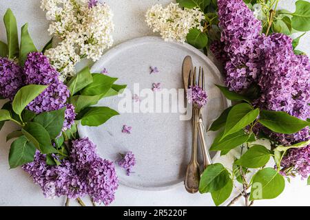 Top view of place setting with vintage ceramic dinnerware with fresh lilac flowers on white surface Stock Photo