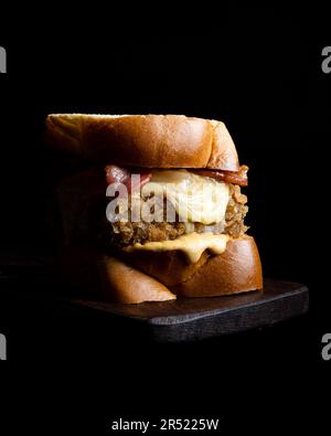 Appetizing burger with fresh buns and cheese served on wooden board on black background Stock Photo