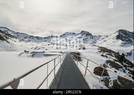 Scenic view of snowy mountains with frozen peaks and long footbridge going through winter nature in Pyrenees under cloudy gloomy sky Stock Photo