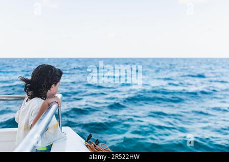 Side view of unrecognizable girl in casual clothes enjoying fresh air while standing on ship deck floating sea water during sunny day Stock Photo