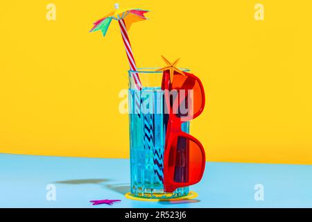 Front view of composition of glass of blue liquid with straw and stylish red eyeglasses placed on bright blue and yellow background in studio Stock Photo