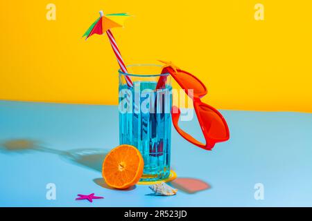 Front view of composition of glass of blue liquid and straw with stylish red eyeglasses placed on bright blue and yellow background in studio Stock Photo