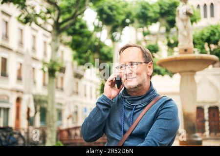 Outdoor portrait of middle age man talking on the phone, wearing glasses and blue sweatshirt, holding smartphone next to ear Stock Photo