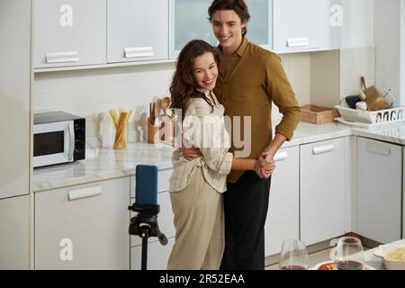 Couple of bloggers filming themselves dancing in kitchen for family vlog Stock Photo