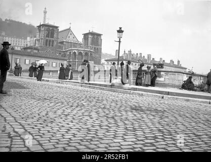 People walking in a paved street in Lyon. Next to Cathedral Saint Jean Baptiste. Beginning of 20th century. Old photograph digitized from glass plate Stock Photo