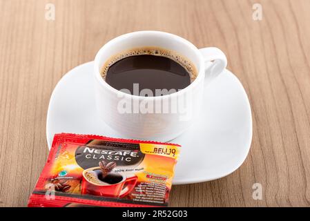 Moscow, Russia, May 31, 2023: Original sachet of Nescafe classic coffee and coffee in a white cup on a wooden background. Copy space. Stock Photo