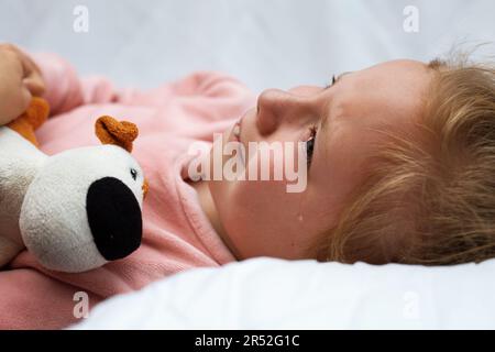 Portrait of little crying girl little rolling tears weeping emotion, Closeup young girl hurt in pain crying in white bed copy space. Stock Photo