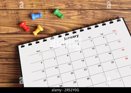 Colorful push pins scattered near a monthly desktop calendar on a wooden table. Concept of time management, office schedule and meetings Stock Photo