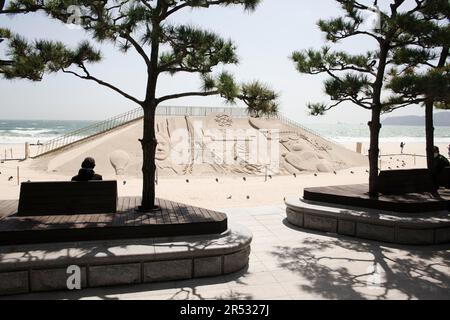 Sand sculpture for the World Expo 2030 in Busan, South Korea, World Expo, city by the sea, Haeundae beach, people on bench under trees, visitors Stock Photo