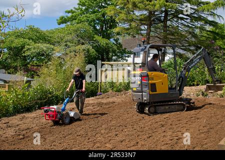 Gower Wales UK May 2023 Machinery preparing ground for replacement grass lawn. Mechanical digger and rotavator in use. Trees and bushes in background. Stock Photo