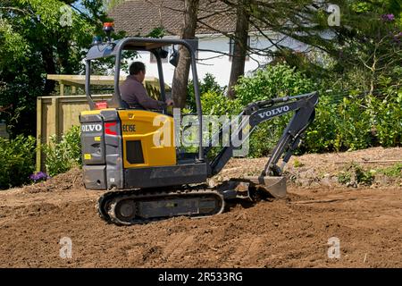 Gower Wales UK May 2023 Machinery preparing ground for a replacement grass lawn. Mechanical digger levelling the soil.Trees and bushes in background. Stock Photo