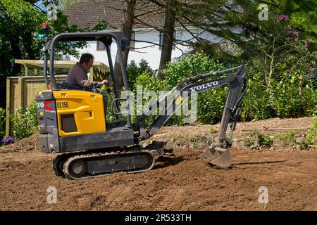 Gower Wales UK May 2023 Machinery preparing ground for a replacement grass lawn. Mechanical digger levelling soil.Trees and bushes in background. Stock Photo