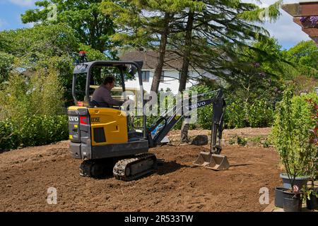 Gower Wales UK May 2023 Machinery preparing ground for a replacement grass lawn. Mechanical digger levelling soil.Trees and bushes in background. Stock Photo