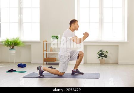 Fit young man doing forward lunge exercise on yoga mat during fitness workout at home Stock Photo