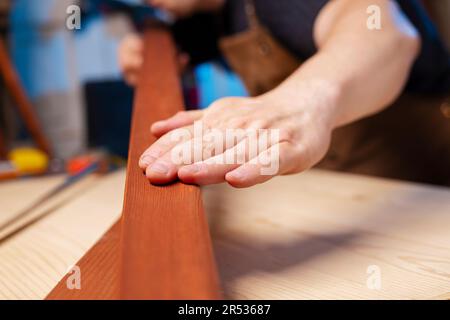 A carpenter checking smoothness of wood material. Woodworker preparing planks Stock Photo