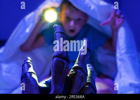 Scared boy with flashlight hides under blanket from the hand of scary monster Stock Photo