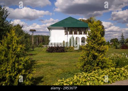 Monastic cells, in a coniferous garden, a white refectory building,a stork's nest on the left, an old well on the right.Forest on the blue sky horizon Stock Photo