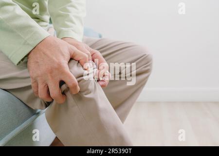 Elderly man suffering from knee pain sitting on sofa at home Stock Photo