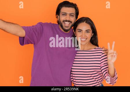 Happy loving eastern young couple taking selfie together on orange Stock Photo