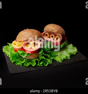 Sandwiches with ham, cheese, tomatoes, lettuce, and barley round bun isolated on black background Stock Photo