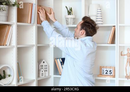 Young man taking book from shelf at home Stock Photo