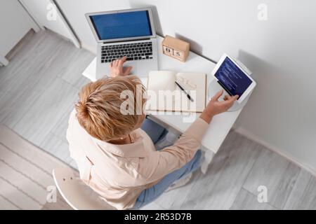 Mature female programmer working with tablet computer and laptop at home Stock Photo
