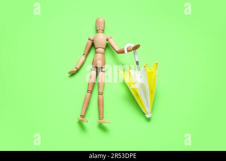 Creative composition with wooden mannequin and mini umbrella on green background Stock Photo