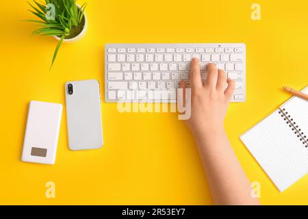 Female programmer using computer keyboard with mobile phone on yellow background Stock Photo