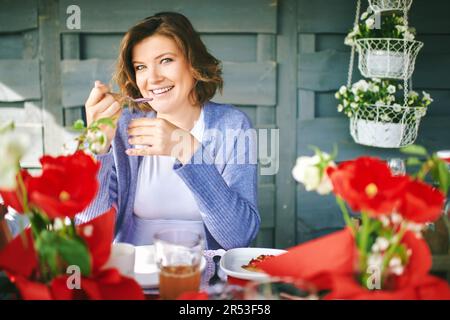 Portrait of happy young woman eating yogurt at the table, easter breakfast Stock Photo