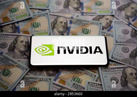 Nvidia logo seen on smartphone which is placed on pile of US dollar bills. Concept. Selective focus. Stafford, United Kingdom, May 31, 2023 Stock Photo