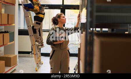 Female supervisor working on logistics with tablet scanner, checking barcodes of merchandise in boxes. Woman employee examining packages with stock products in warehouse depot. Stock Photo