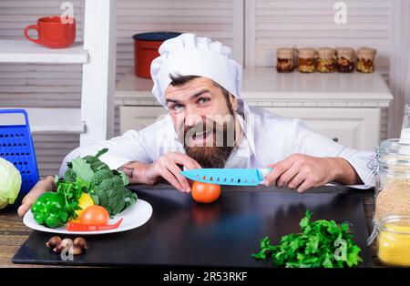 Male chef preparing tasty fresh vegetable salad. Chef with sharp knife cuts tomato. Diet, healthy food cooking, vegetarian concept. Professional chef Stock Photo