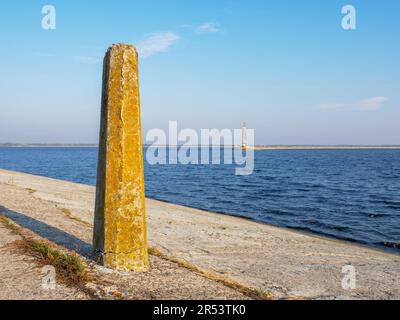 View from the concrete bollard over the old concrete lighthouse on the edge of the Kyiv sea spit, calm blue water, blue sky, and narrow bank strip. Stock Photo