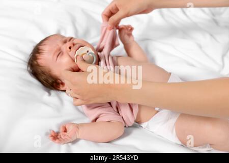 Mother putting clothes on crying daughter on bed, closeup Stock Photo