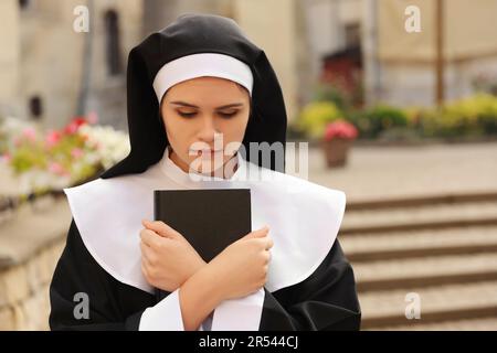 Young nun with Bible outdoors on city street Stock Photo