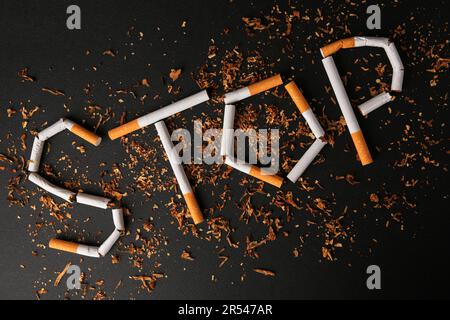 Word Stop made of broken cigarettes on black background, flat lay. Quitting smoking concept Stock Photo