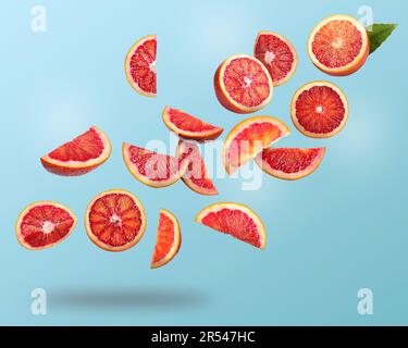 Many cut tasty Sicilian oranges falling on light blue background Stock Photo
