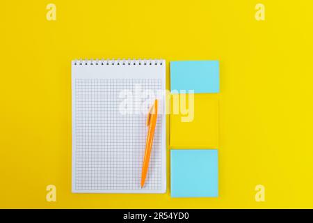 Top view of open notebook with pen and blank pages next to  colorful stickers on yellow background. Back to school. Copy space Stock Photo