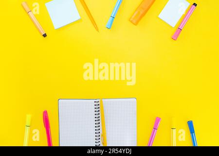 Open notebook with pen, marker and blank pages next to colorful stickers on yellow background. Back to school. Copy space Stock Photo