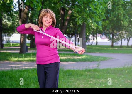 Portrait of a beautiful elderly woman doing exercises. Portrait of fit mature woman smiling on park background. Athletic senior woman Stock Photo