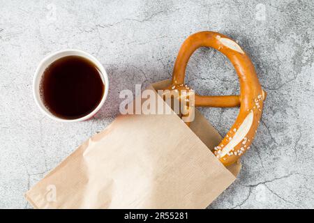Pretzel wrapped in wrapping paper with drink next to it on stone table Stock Photo