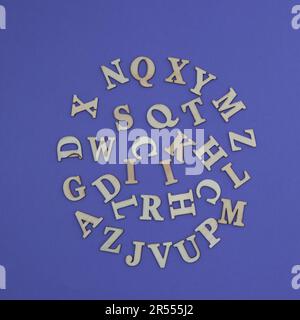 Various wooden letters of the alphabet arranged in a circle on a purple background. Minimal aesthetic scene. Stock Photo