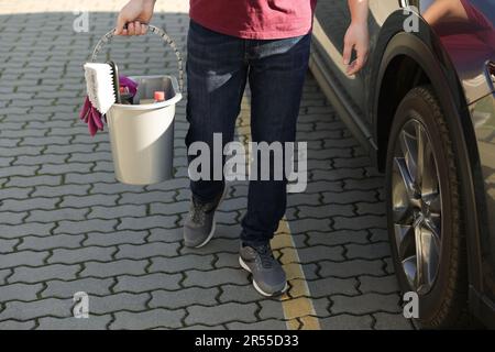 Man holding bucket with car cleaning products outdoors, closeup Stock Photo